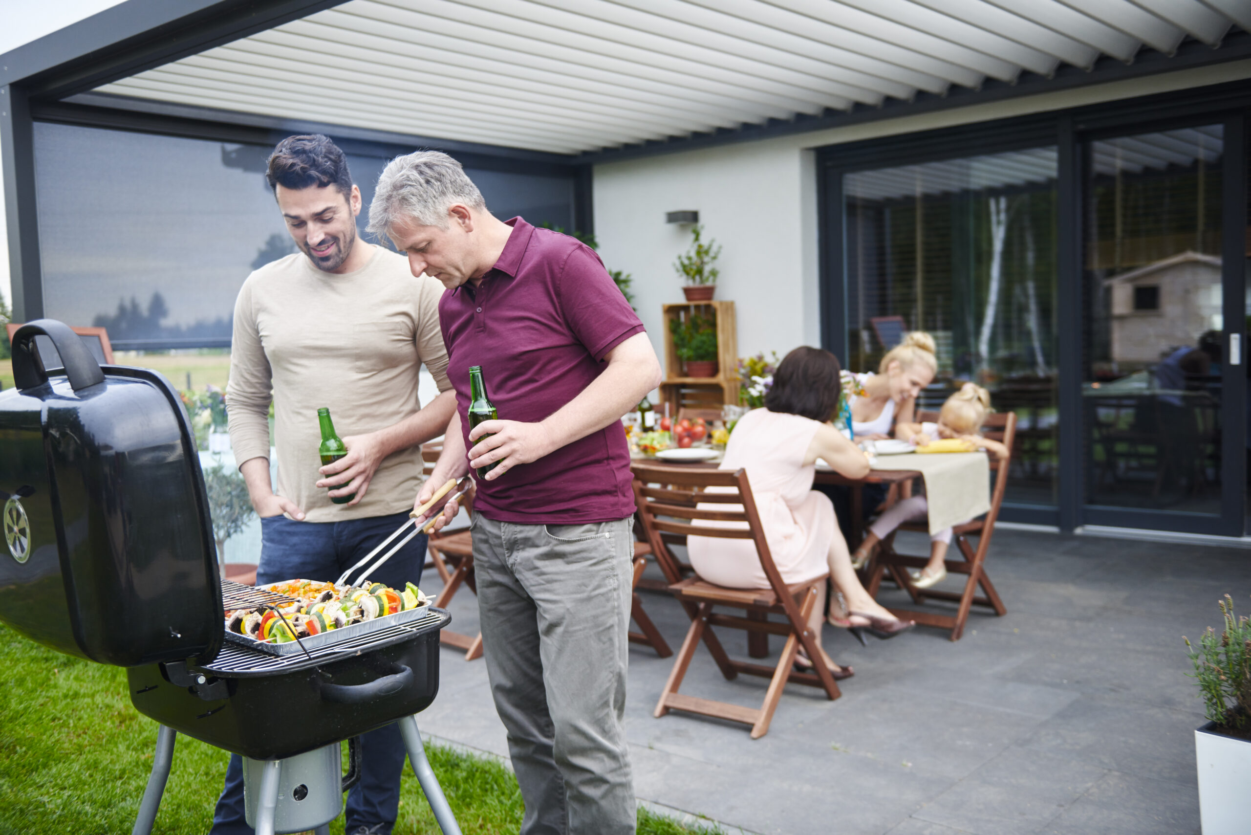 Mature and mid adult man barbecuing at family lunch on patio - Shade Space